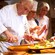 A chef drizzling oil into a wooden salad bowl during a cooking class